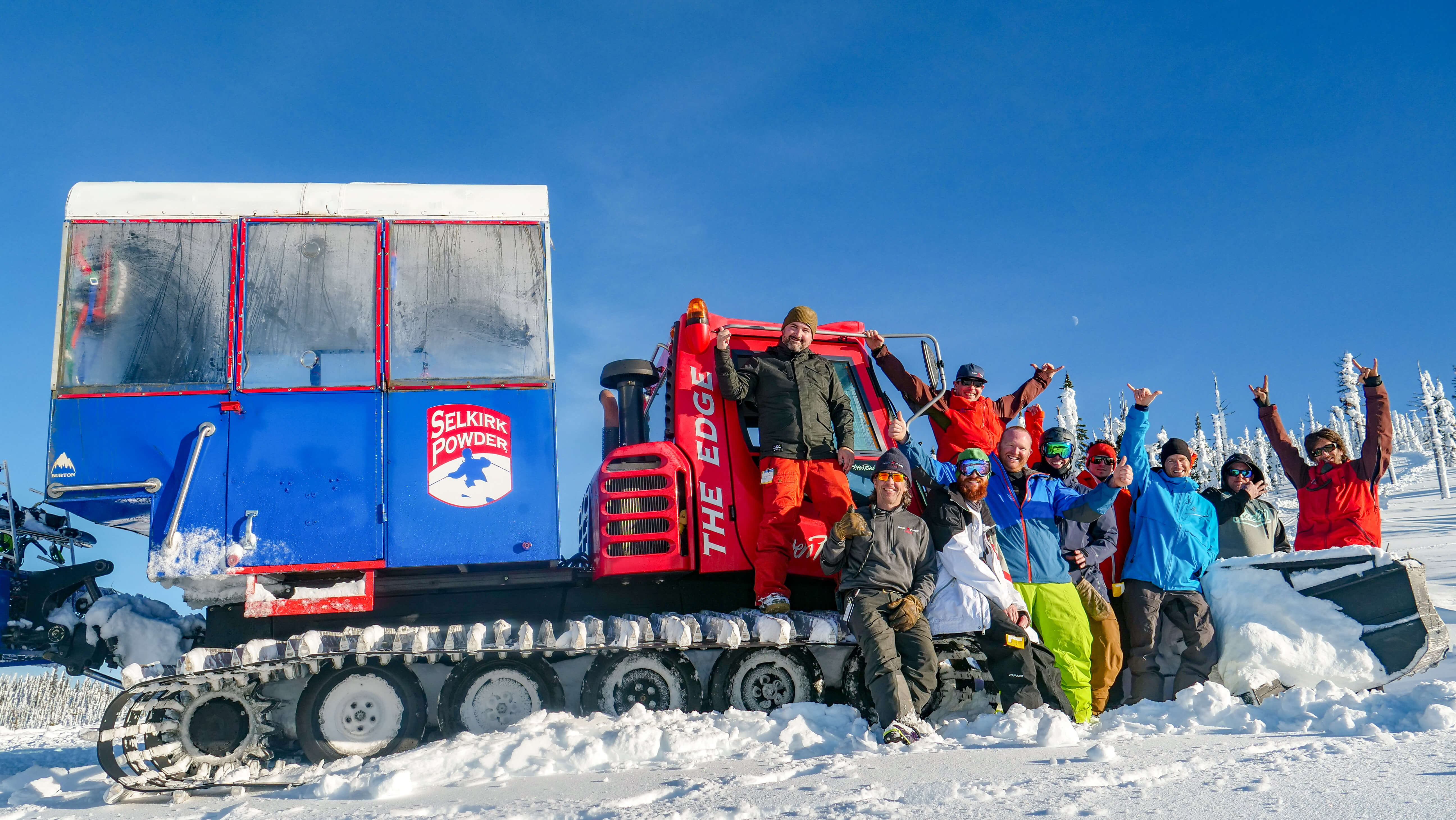 A happy group cheers in front of a snowcat