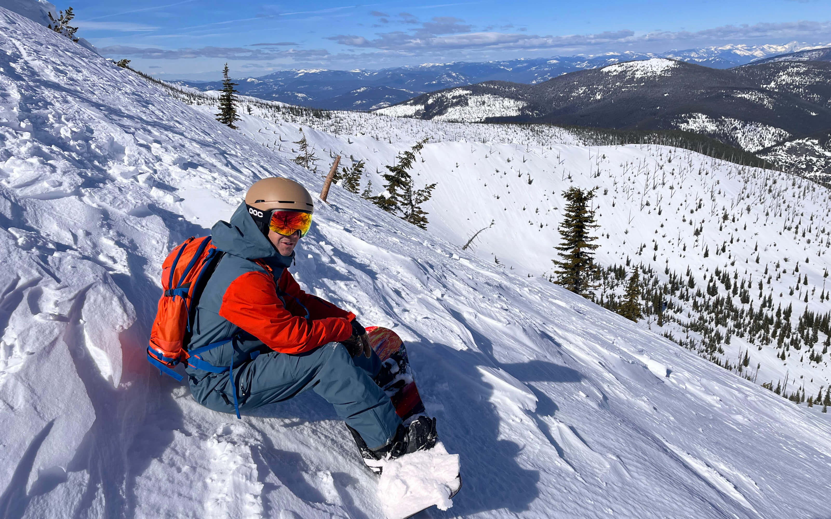 A snowboarder sits at the top of a backcountry run